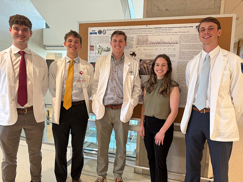 Six medical students stand in front of their hallway research posters.